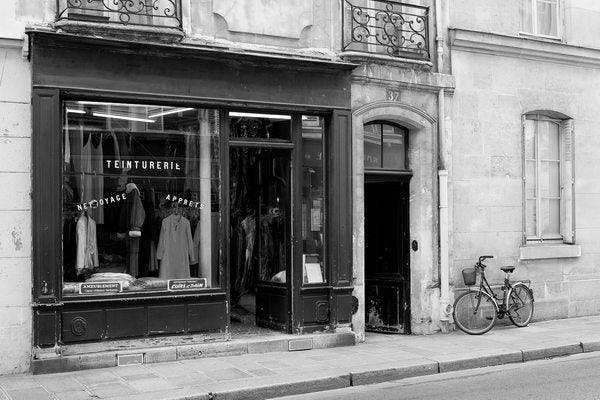 Black and white photo of vintage storefront with hanging coats and bicycle by entrance