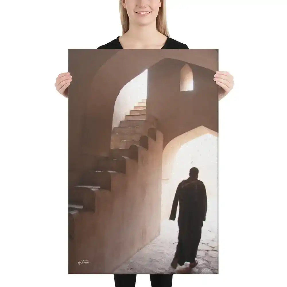 Canvas print of person walking in arched stone hallway with sunlight and staircase