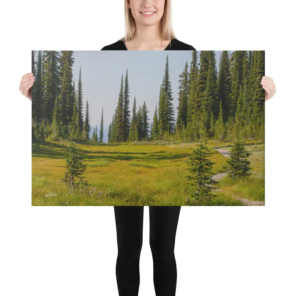 Woman holding large nature canvas print with forest meadow, tall evergreens, and mountain path — perfect wall art for home decor.