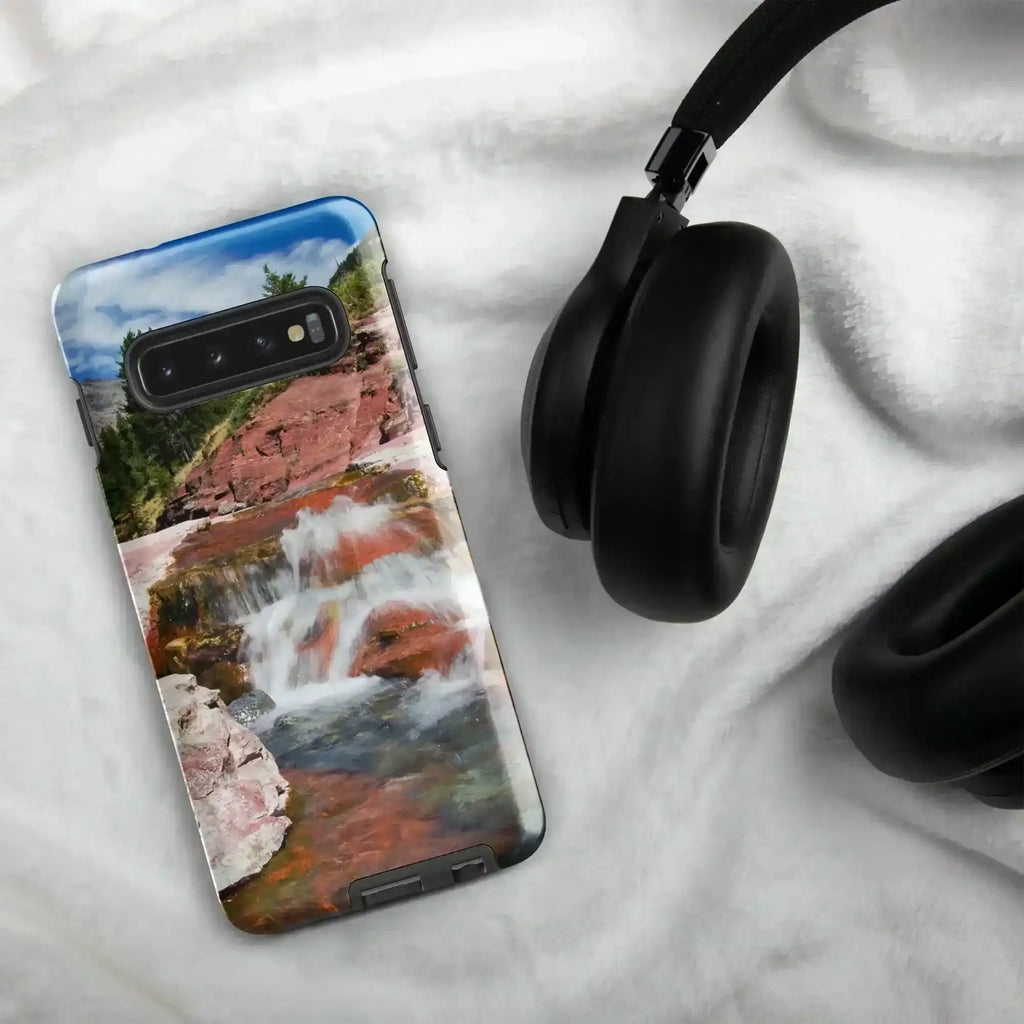Samsung Galaxy S10 case with waterfall landscape, glossy finish, on white fabric next to headphones