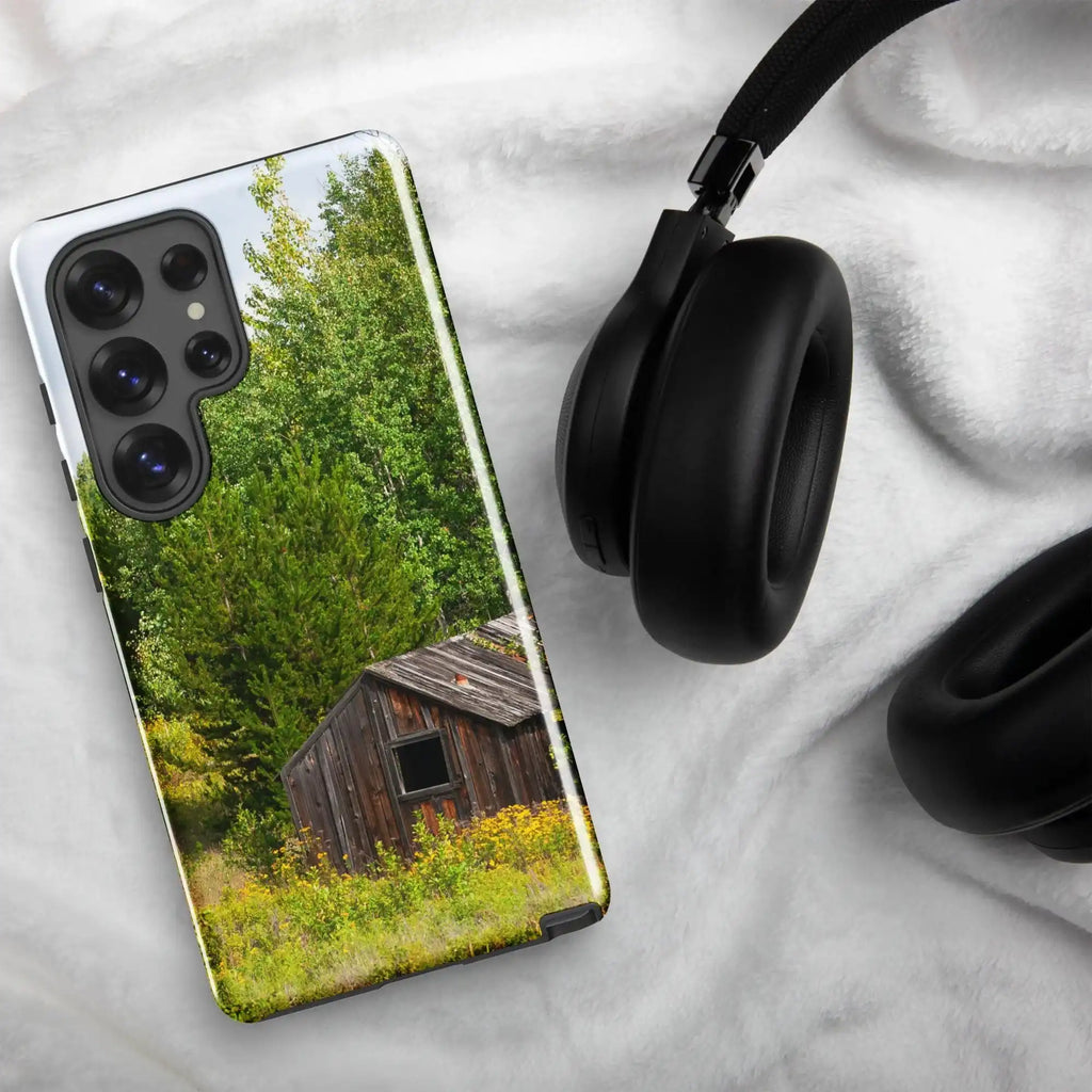 Samsung Galaxy S25 Ultra case with rustic cabin photo design, displayed on white fabric next to black headphones.