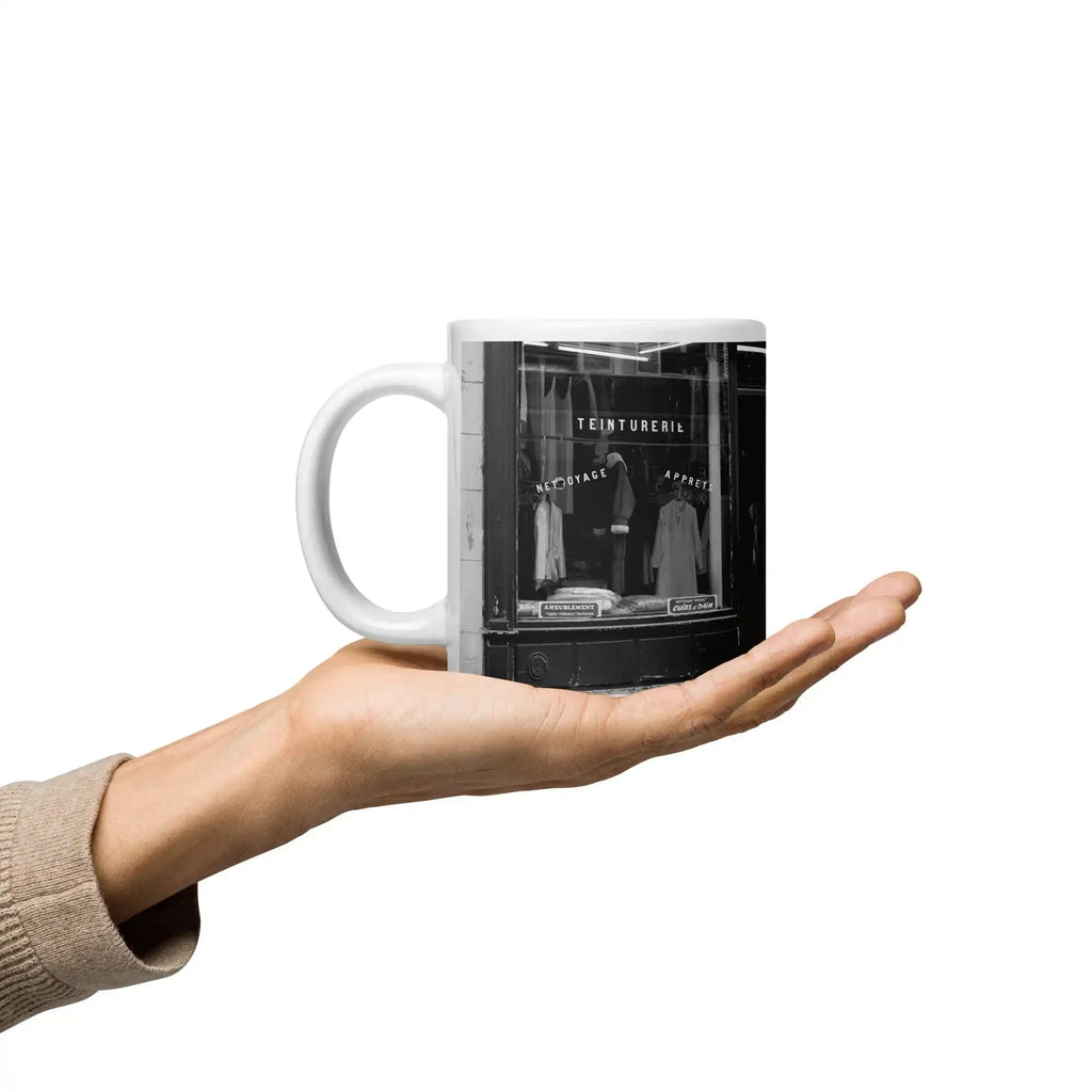 Person holding a white ceramic mug with a black and white vintage storefront photo print